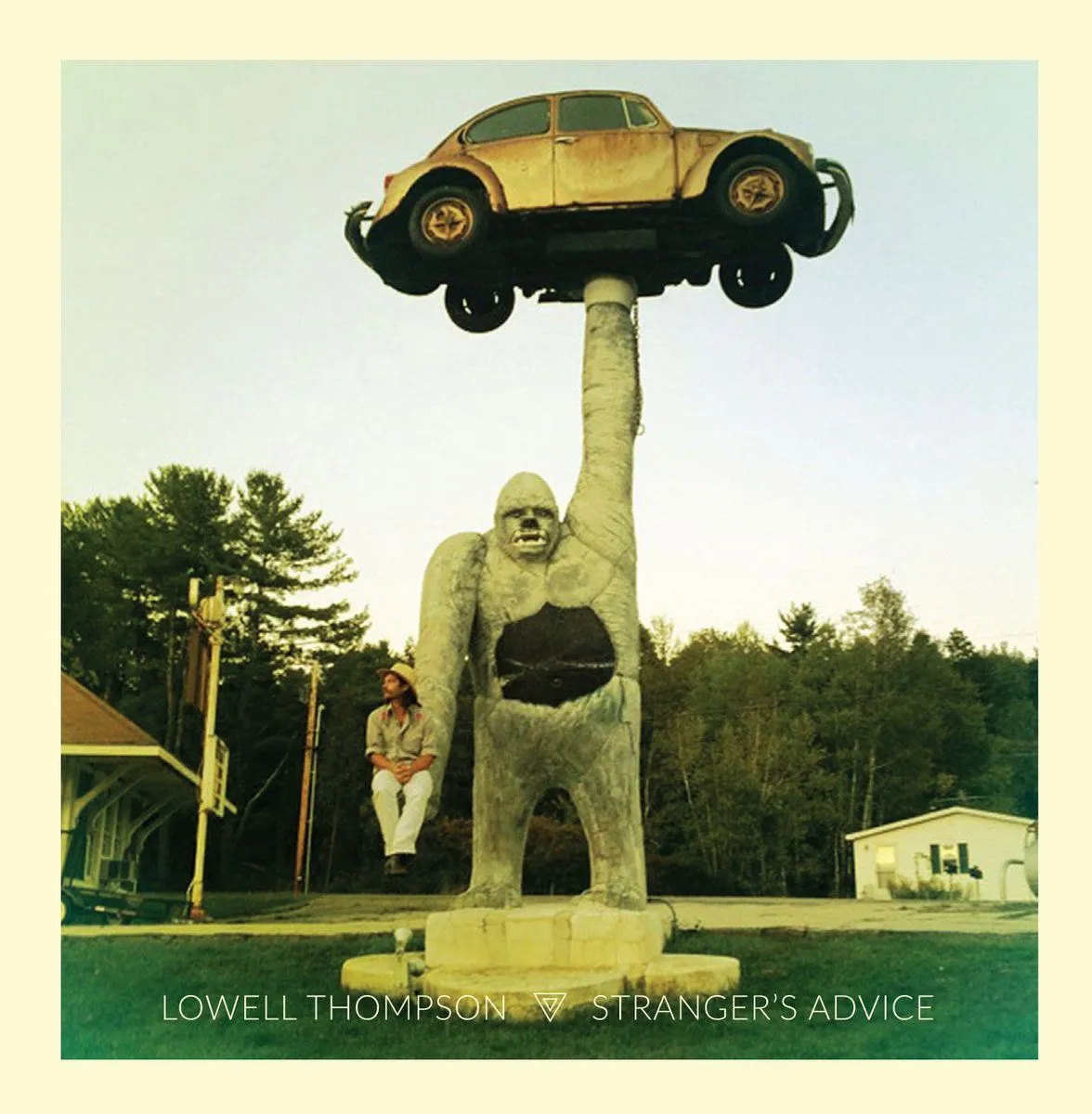 Lowell Thompson sitting beneath a roadside gorilla statue that holds a Volkswagen Beetle above its head.